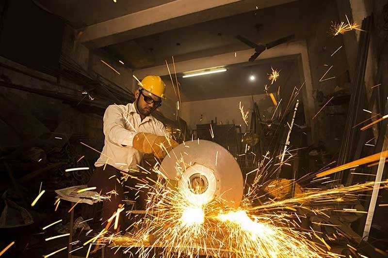 Worker grinding metal with sparks, wearing protective gear